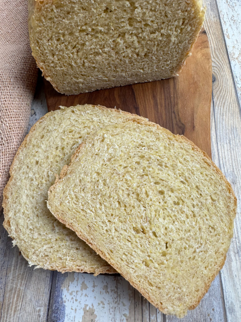 Cut yeasted honey cornbread loaf on a wooden board, two slices in front showing a soft yellow-tinged crumb, on weathered wood.