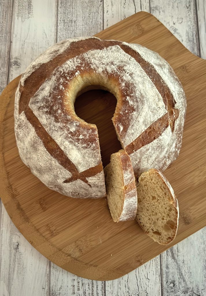 Floured pompe à l’huile ring with four crossed slashes on a wooden board, two slices cut to show the crumb.
