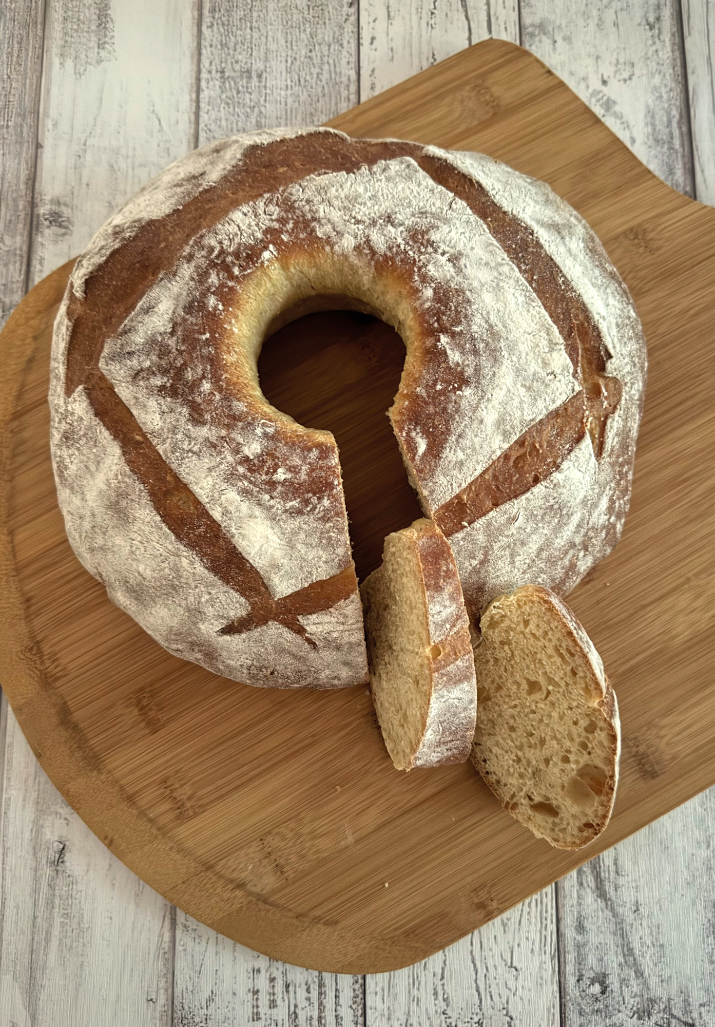 Floured pompe à l’huile ring with four crossed slashes on a wooden board, two slices cut to show the crumb.