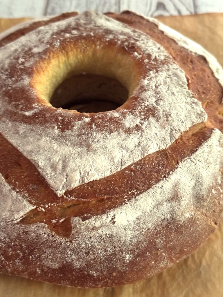 Close-up of the floured top of a pompe à l’huile ring with deep golden slashes around the center hole.
