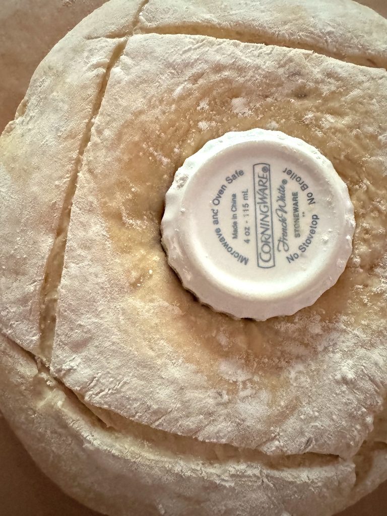 Floured ring scored with four long slashes around a ramekin, ready to bake.