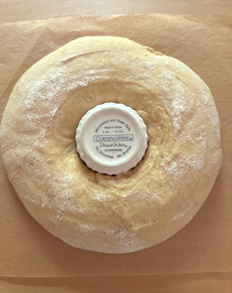 Proofed ring turned out onto parchment with a white ramekin in the center.