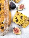 Close-up of a pumpkin fig baguette slice with a golden open crumb and dark fig pieces, beside Brown Turkey fig halves