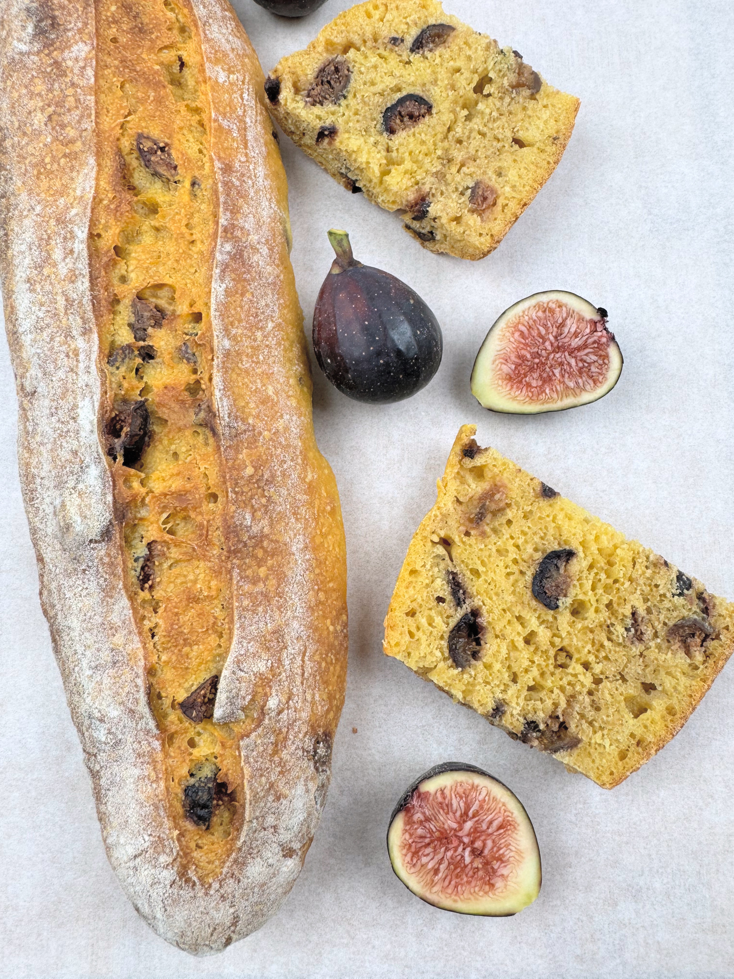 Pumpkin fig baguette with one long score beside two golden slices, a whole fig and two fresh fig halves