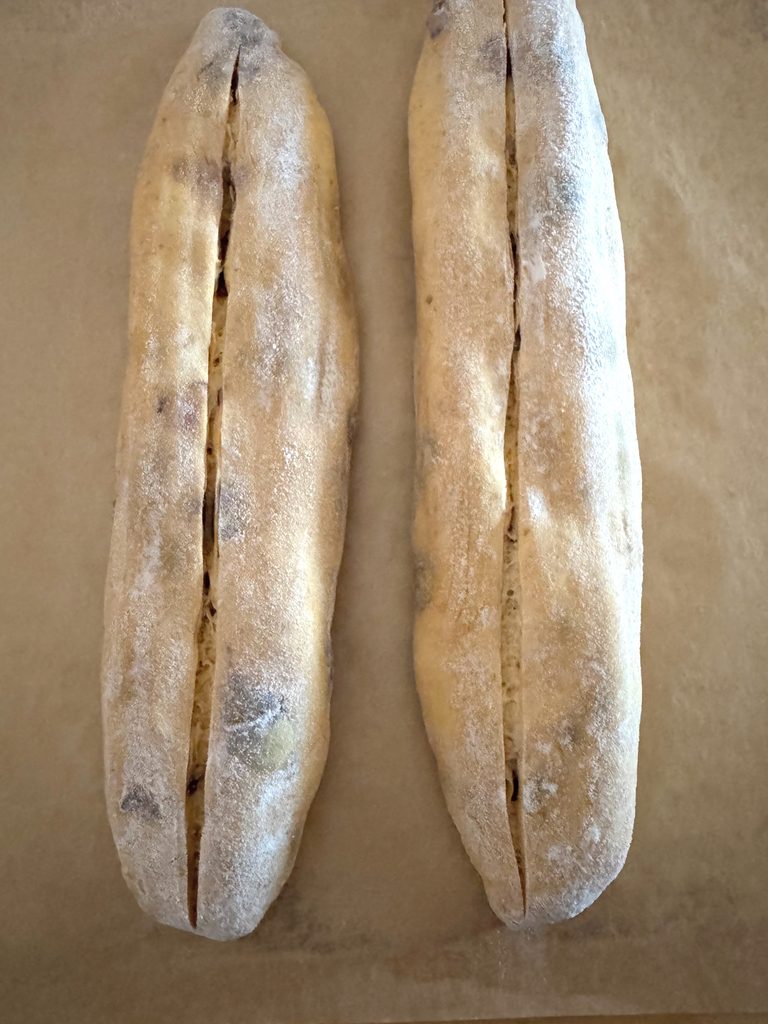 Two scored pumpkin and fig baguettes on parchment, each with one long open score, ready to go into the oven
