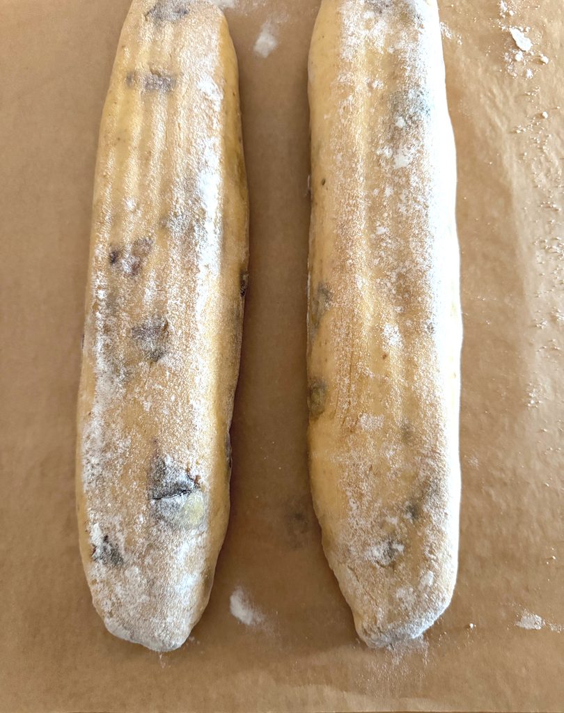 Two shaped pumpkin and fig baguettes dusted with flour, resting on parchment