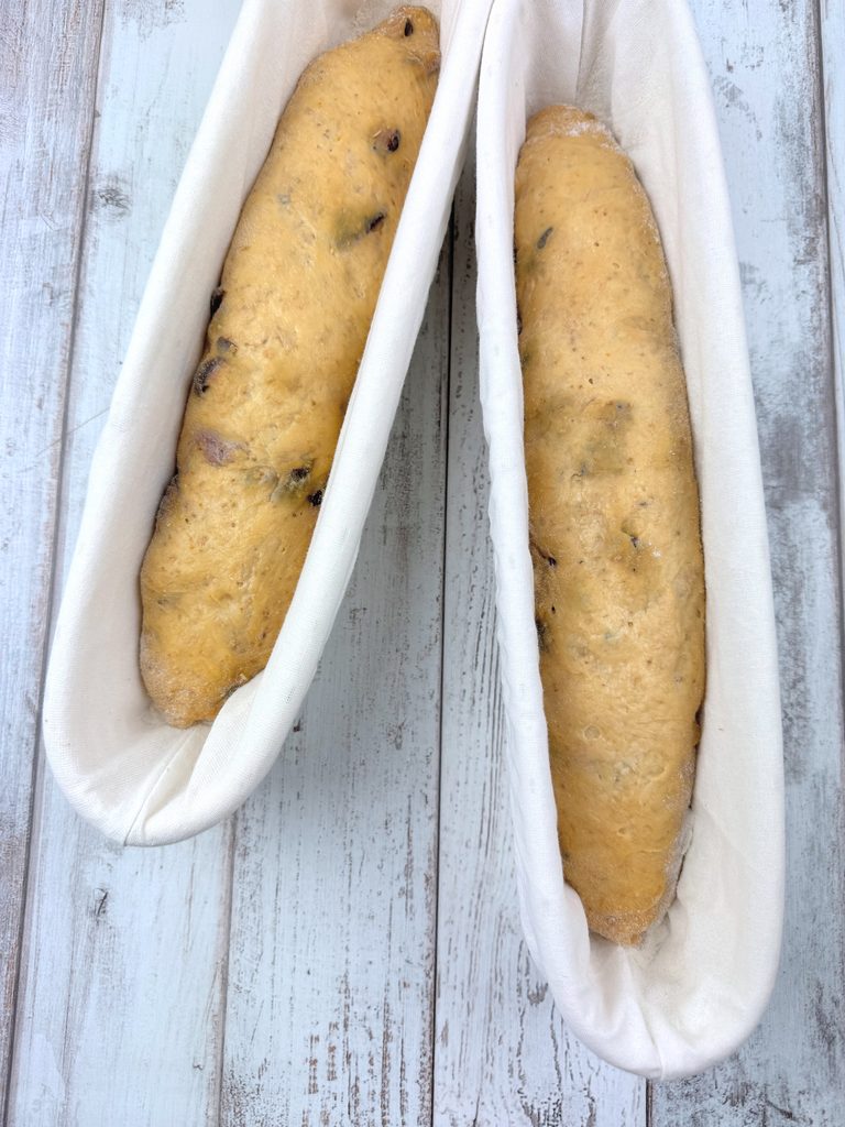 Two shaped pumpkin and fig baguettes proofing in linen-lined 15-inch baguette baskets
