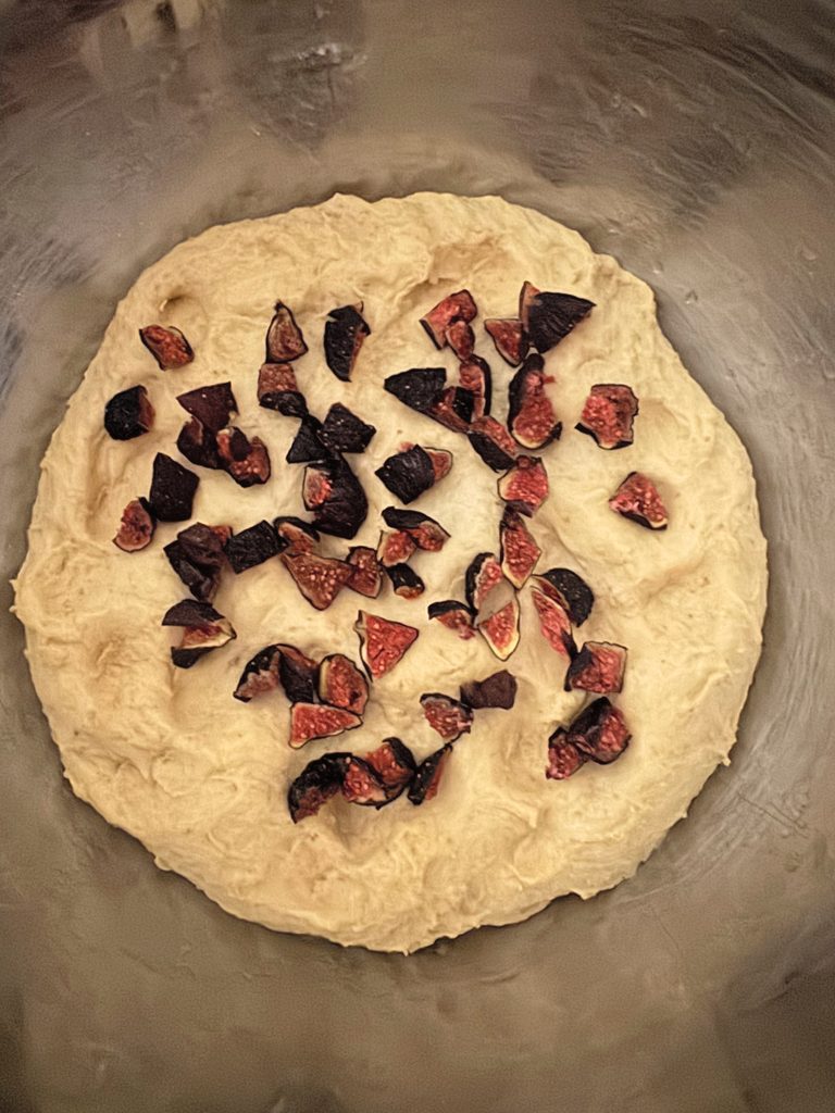 Chopped dried Brown Turkey figs scattered over pale pumpkin dough in a steel mixing bowl, ready to fold in