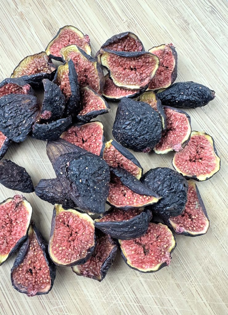 Halved home-dried Brown Turkey figs with dark wrinkled skins and pink seedy centers piled on a wooden cutting board