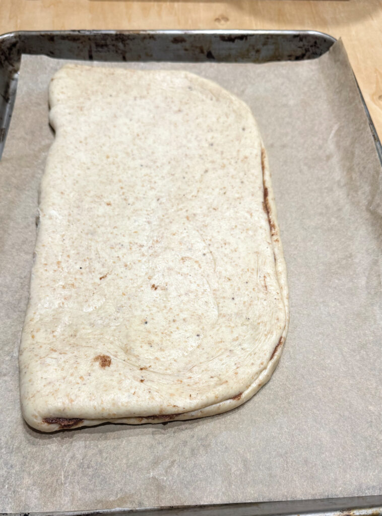 The dough folded in half over the filling into a rectangle, resting on a parchment lined baking sheet.