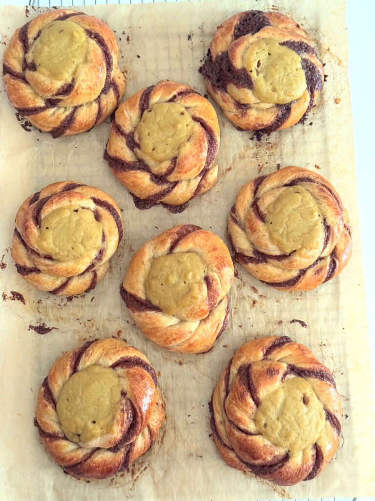 Eight baked Norwegian sun buns on parchment, each a twisted coil with a custard center and cinnamon swirls.