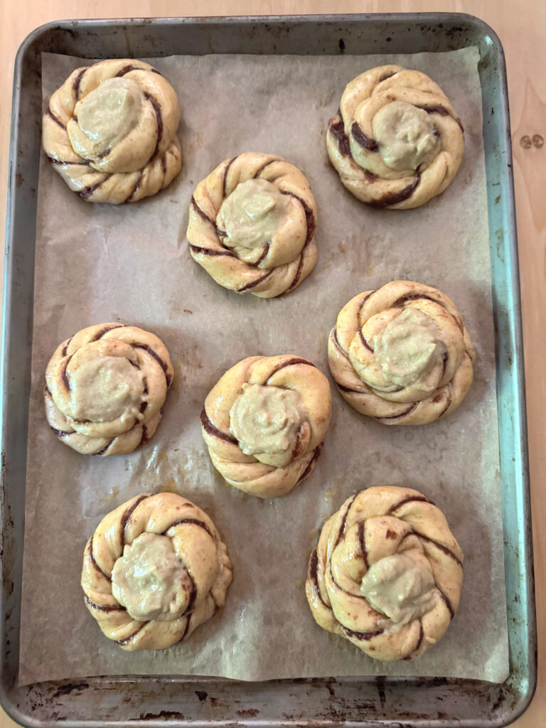 Eight sun buns with vanilla custard spooned into each center, egg washed and ready for the oven.
