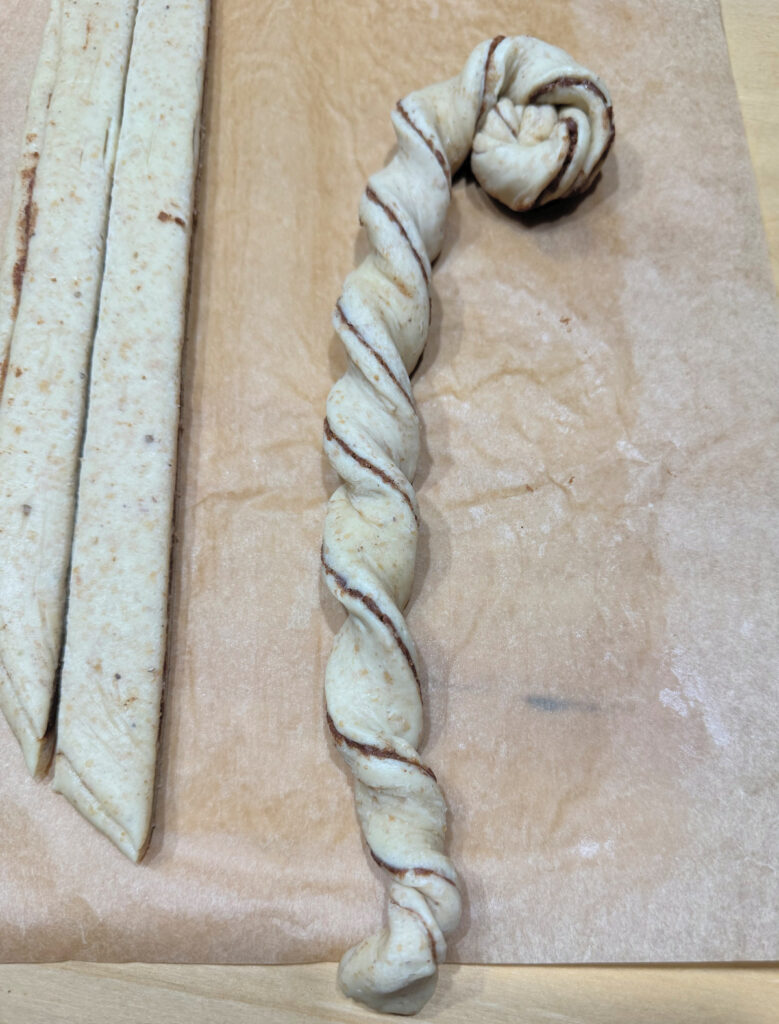 A single dough strip twisted into a long rope and starting to coil at one end.