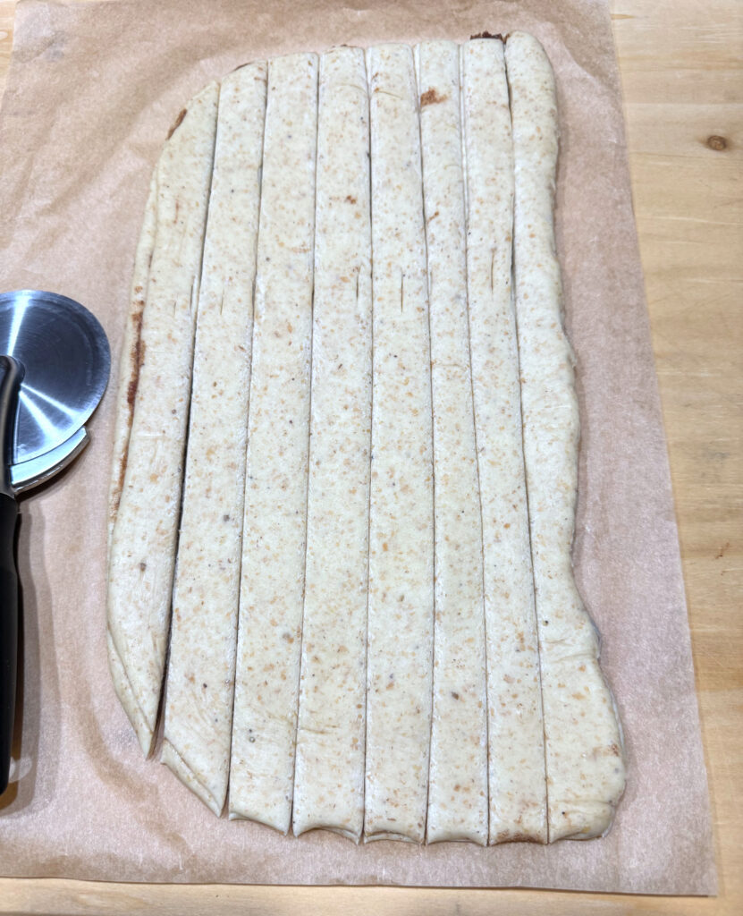 The dough rolled out and cut lengthwise into eight even strips, a pizza wheel resting alongside.