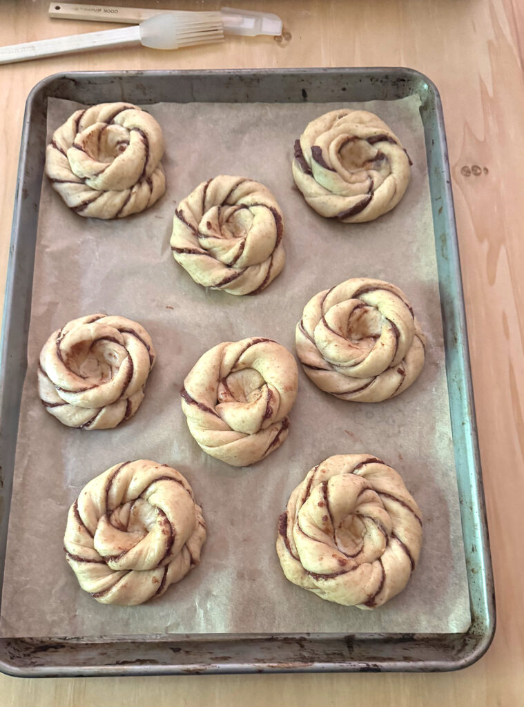 Eight proofed sun buns on a parchment lined sheet, each with an indentation pressed into the center.