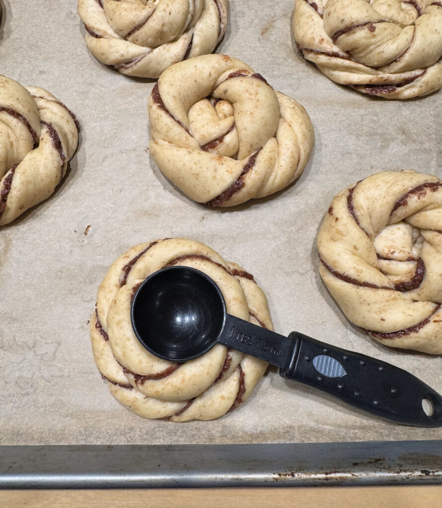 The back of a tablespoon pressing a one inch indentation into the center of a proofed sun bun.