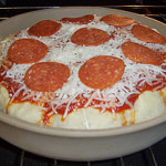 Unbaked deep-dish pepperoni pizza with shredded cheese in a cream stoneware baker on an oven rack.