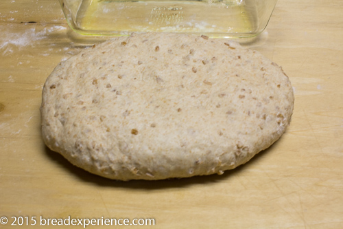 Single piece of cracked wheat dough flattened into an oval on a floured wooden surface.