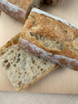 Thick slices of crusty baguette on a wood board, showing an open airy crumb and golden flour-dusted crust.
