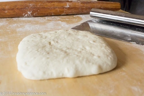 Portion of sourdough dough flattened into a rough square on a floured surface, ready to be cut into strips.