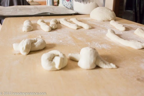 Dough strips in various stages of being shaped. Some loose ropes, some tied into knots, on a floured surface.