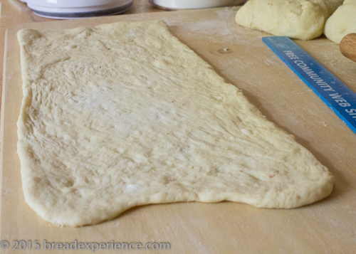 One portion of sourdough dough rolled into a long rectangle on a floured board, ready to be filled.