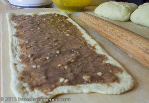 Rolled-out sourdough rectangle spread with a thin layer of ground almond and cinnamon filling, with a lemon and dough pieces nearby.