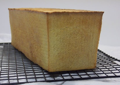 Toast Bread with Teff cooling on a wire rack, with the flat top and square sides of a lidded Pullman loaf